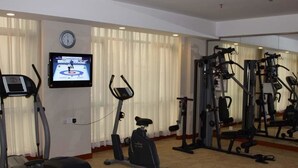 A gym with cardio machines, a TV displaying a sports event, and a mirror reflecting the equipment. - Starshine Hotel (Shenzhen)