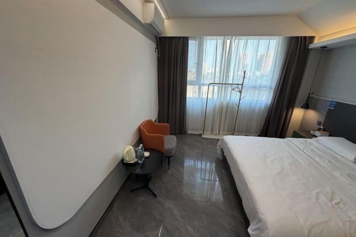 A hotel room with a bed, a desk, a chair, and a window with curtains.