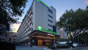 A Holiday Inn Express hotel with a modern design, featuring a prominent green and white logo, and a well-lit entrance. - Vienna Hotel (Shanghai)