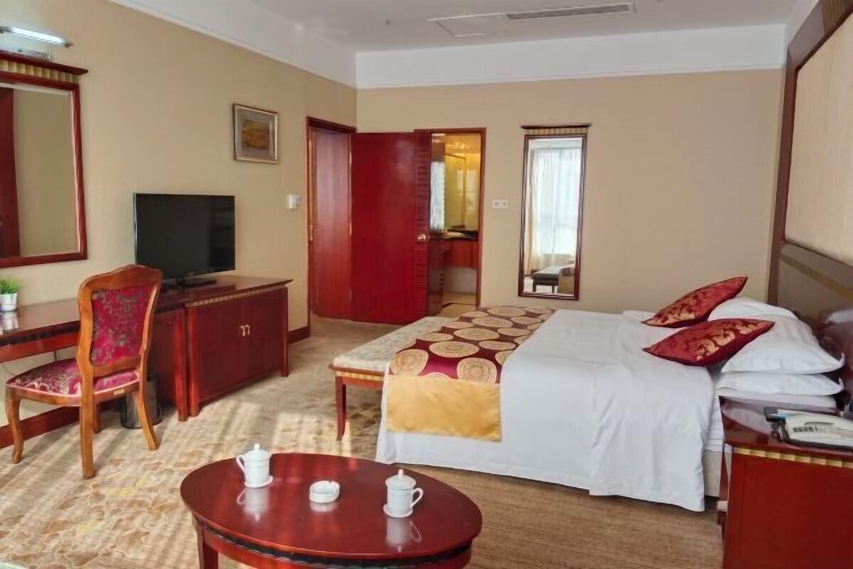 A hotel room with a bed, a desk with a television, a chair, and a small table with cups.
