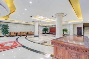 A lobby with a central reception desk, seating area with sofas, and a large potted plant. - Mizhou Hotel (ZHUCHENG)