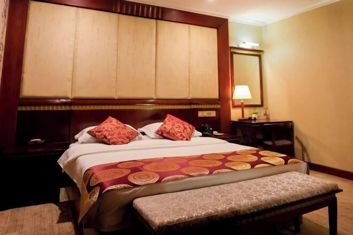 Habitación de hotel con una cama grande, una mesita de noche, un banco, un espejo y una lámpara.