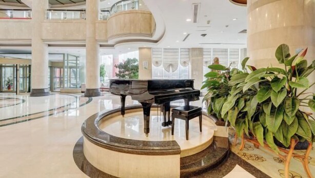 A spacious lobby with a grand piano, large columns, and potted plants. - Mizhou Hotel (ZHUCHENG)
