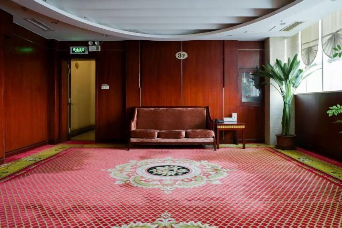Habitación de hotel con sofá, una mesita, una planta en maceta y alfombra estampada.