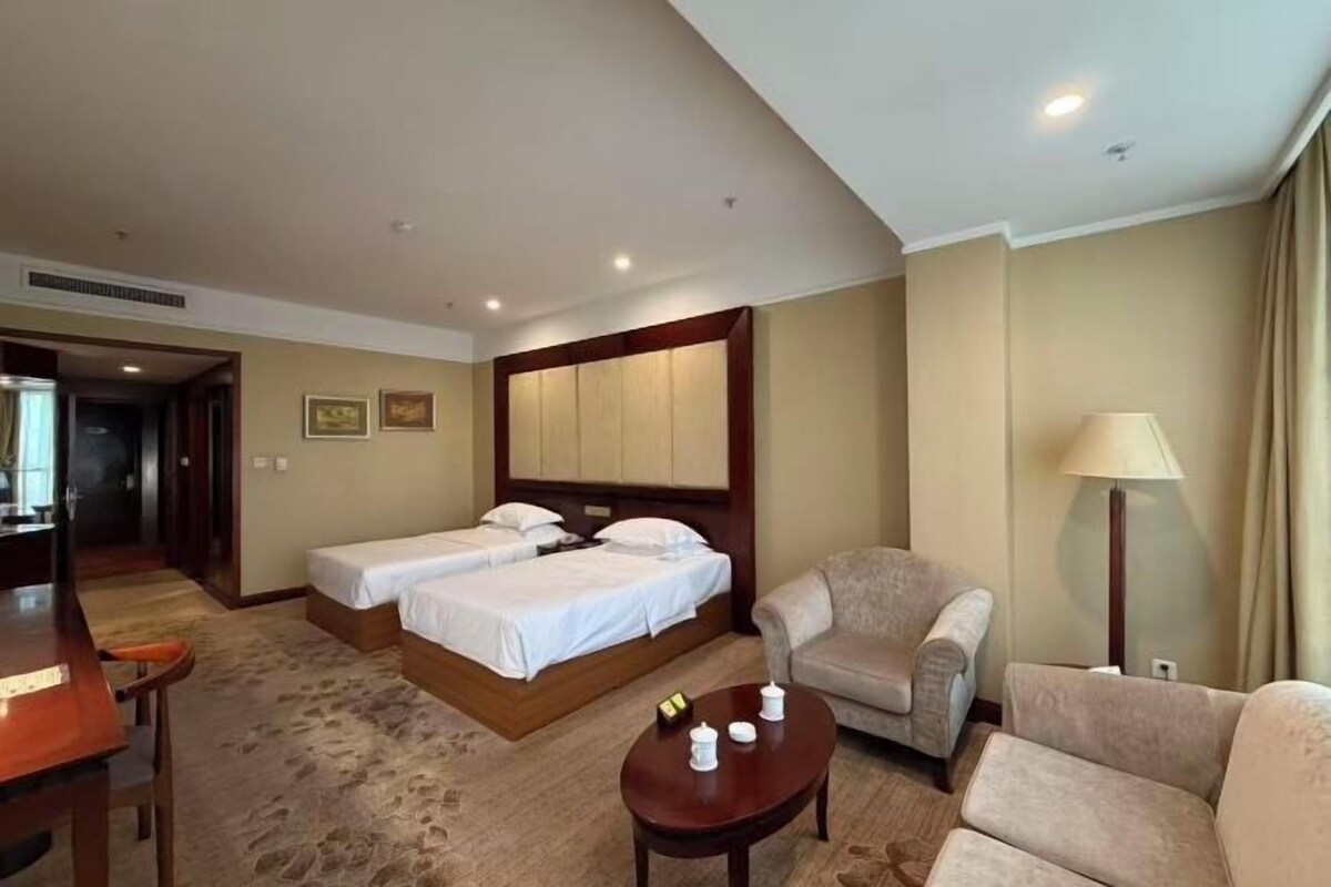 A hotel room with two beds, a sofa, a coffee table, and a lamp.