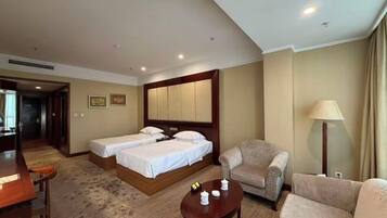 A hotel room with two beds, a sofa, a coffee table, and a lamp.
