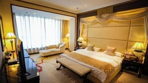 A hotel room with a large bed, a desk with a computer, a chair, and a bedside table with lamps. - Mizhou Hotel (ZHUCHENG)
