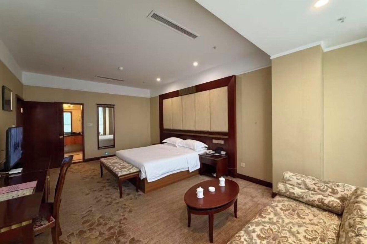 A hotel room with a bed, a desk, a chair, a sofa, and a television.