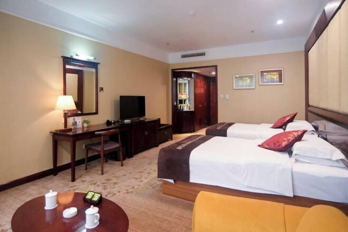 Habitación de hotel con dos camas, un escritorio con televisor, una mesa de centro con tazas y un espejo.