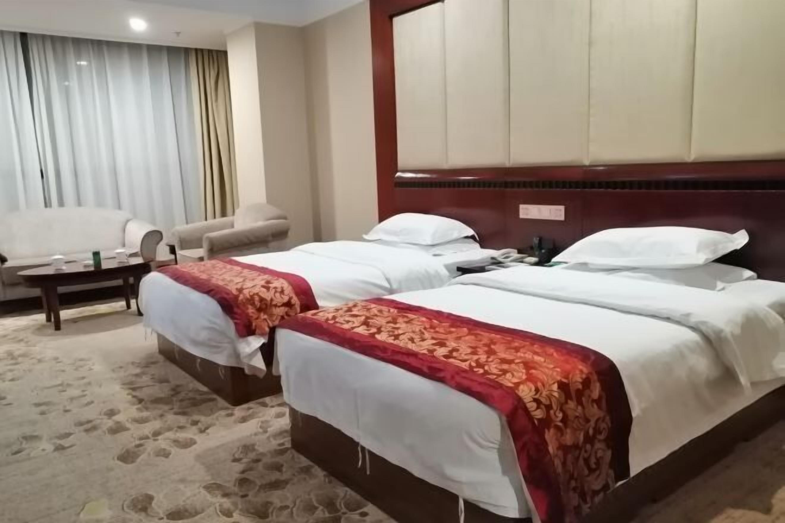 A hotel room with two beds, a sofa, a coffee table, and a large window with curtains.