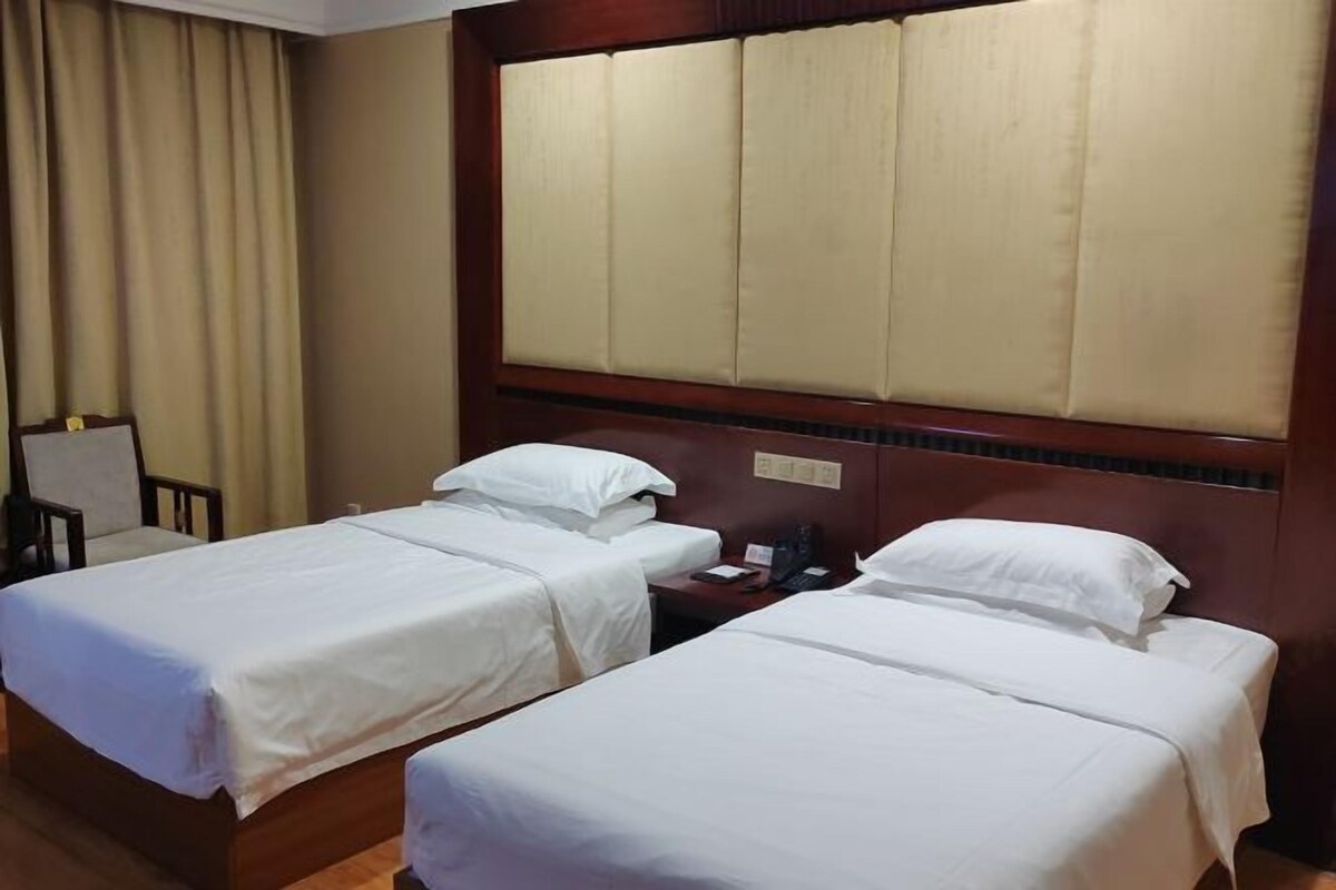 A hotel room with two single beds, a wooden headboard, a nightstand, and a chair.