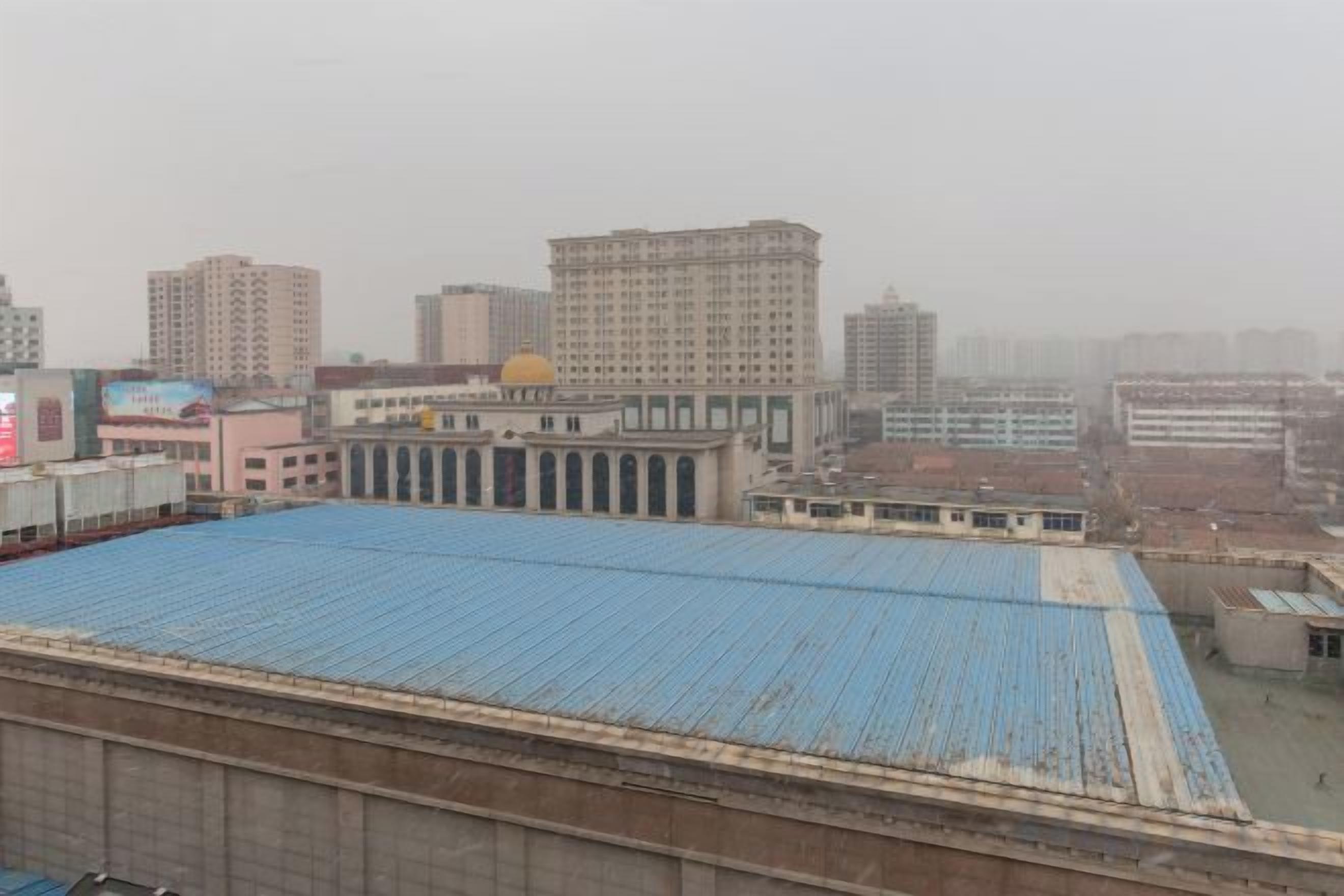 Un edificio grande con techo azul, rodeado de otros edificios y un cielo brumoso.