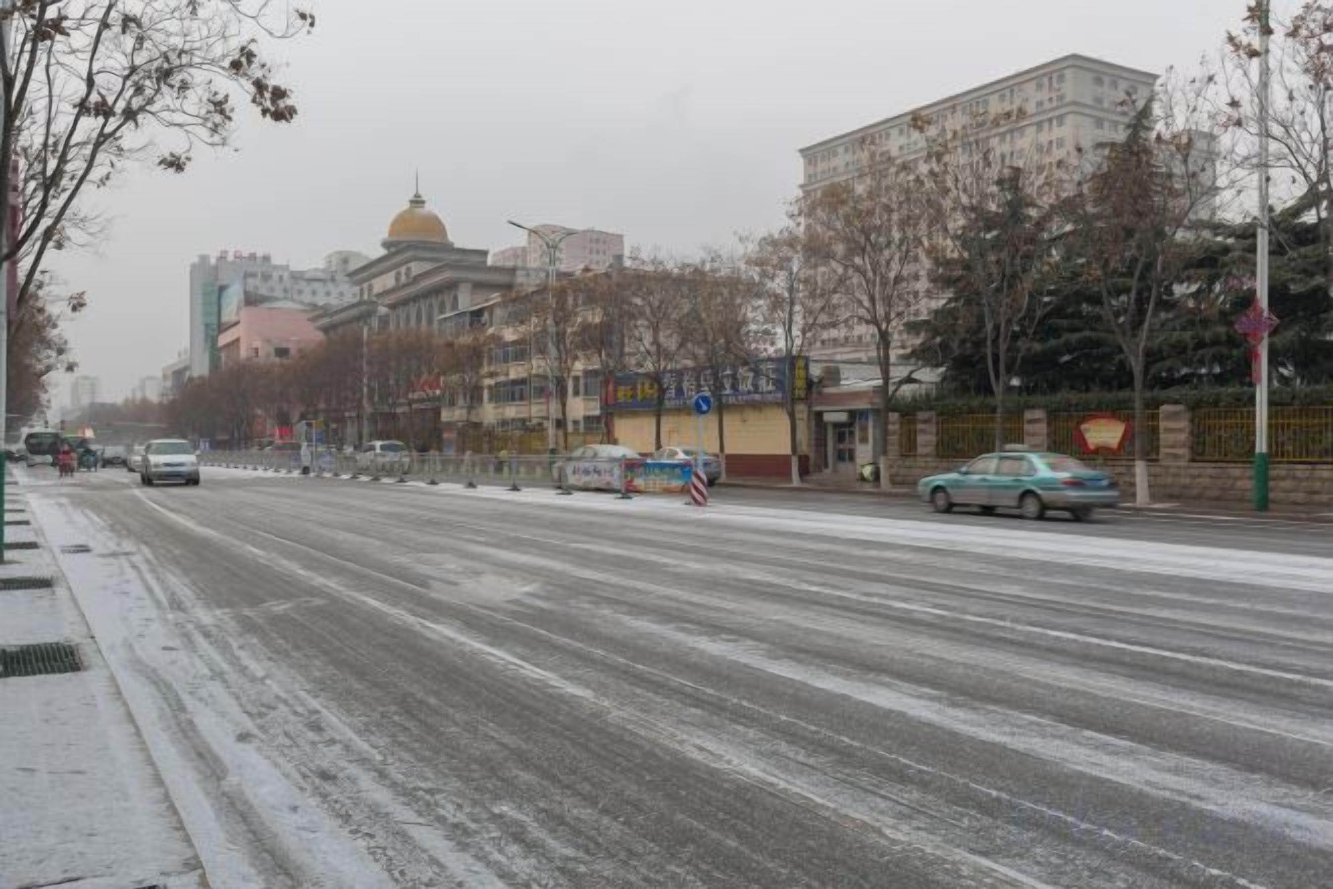 A snow-covered road with buildings and trees.