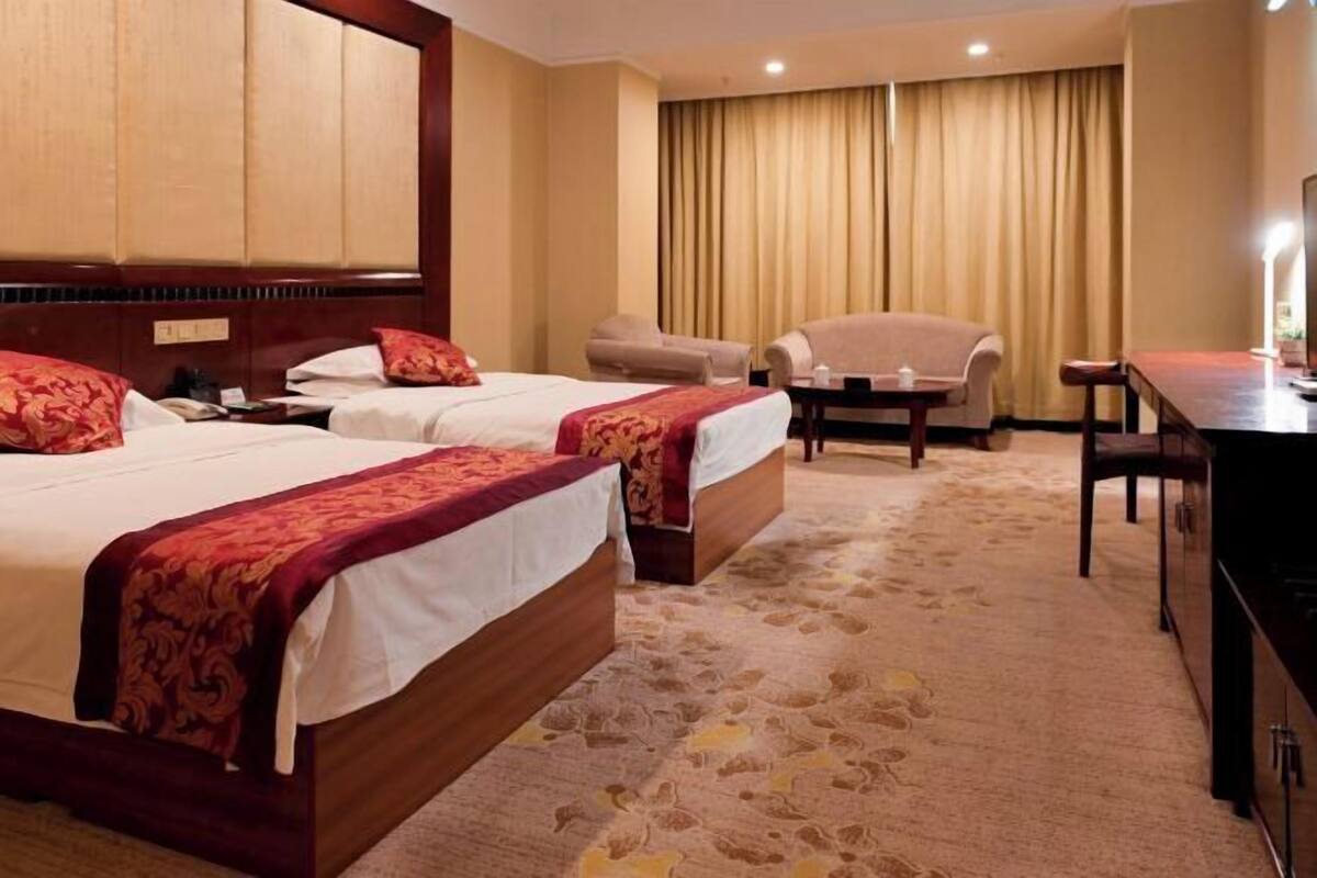 Habitación de hotel con dos camas, un escritorio, una silla y un televisor.
