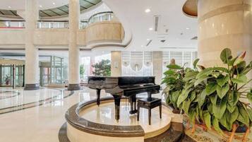 A spacious lobby with a grand piano, large columns, and potted plants.