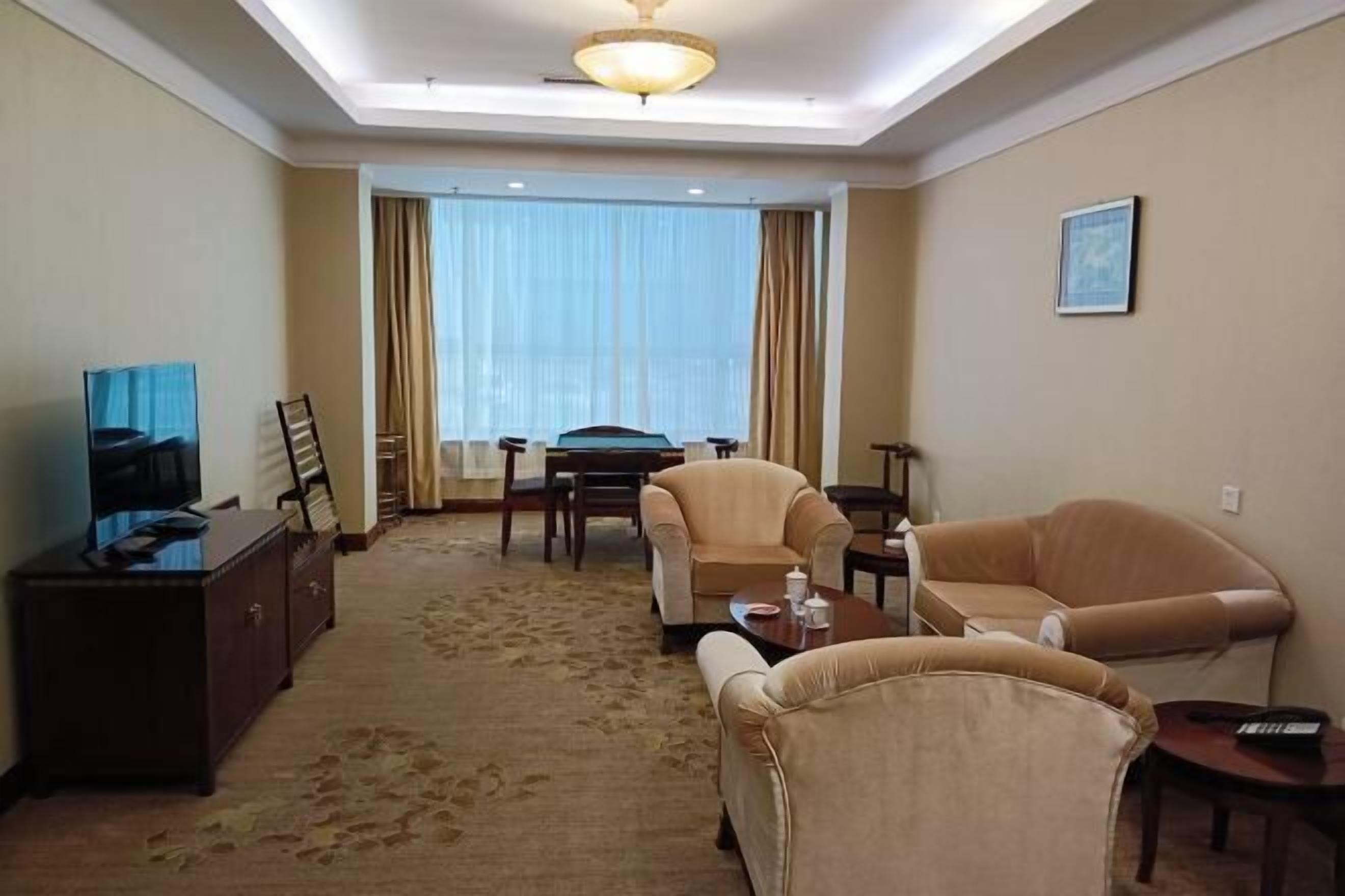 A hotel room with a large window, a television, a desk, and two armchairs.