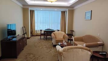 A hotel room with a large window, a television, a desk, and two armchairs.