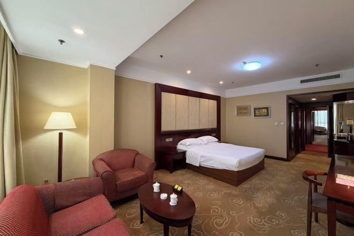 A hotel room with a bed, a desk, a chair, a sofa, and a lamp.