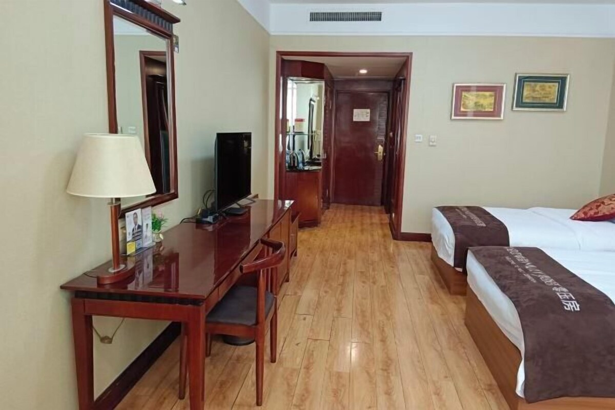 A hotel room with a wooden desk, a television, a bed with a brown blanket, and a mirror on the wall.