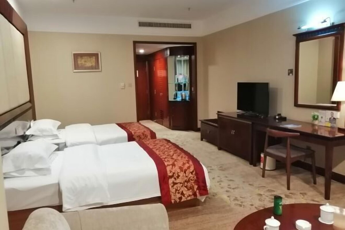 A hotel room with two beds, a desk, a television, and a dining area with a table and chairs.