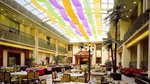 A spacious indoor dining area with multiple tables set for guests, a high ceiling with colorful drapes, and a central decorative element resembling a traditional Asian pavilion. - Mizhou Hotel (ZHUCHENG)