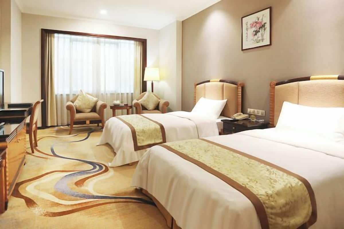 A hotel room with two beds, a desk, a chair, a lamp, and a painting on the wall.