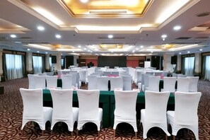 A conference room with rows of white chairs, a green table, and a stage at the front. - Royal Prince Hotel (Quanzhou)
