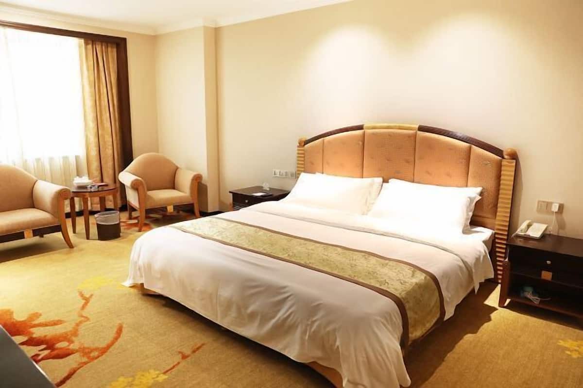 A hotel room with a large bed, a sofa, a small table, and a nightstand.
