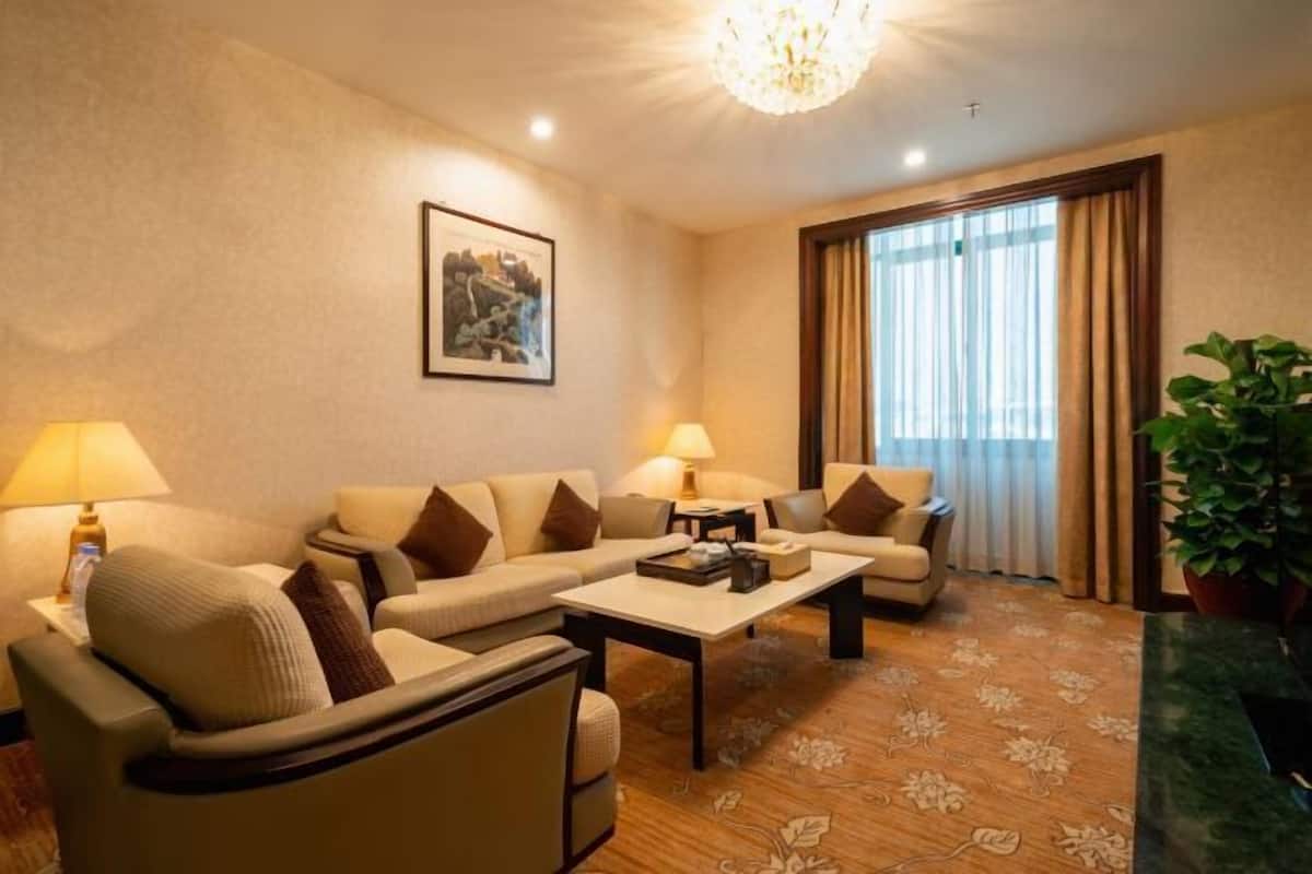 A hotel room with a sofa set, a coffee table, a lamp, a picture on the wall, and a window with curtains.