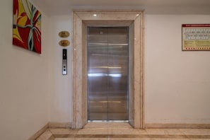 An elevator with a marble frame, a control panel, and a safety sign on the wall. - Royal Prince Hotel (Quanzhou)