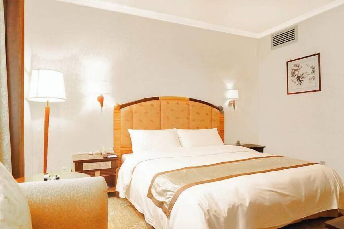 A hotel room with a large bed, bedside tables, a lamp, and a framed artwork on the wall.