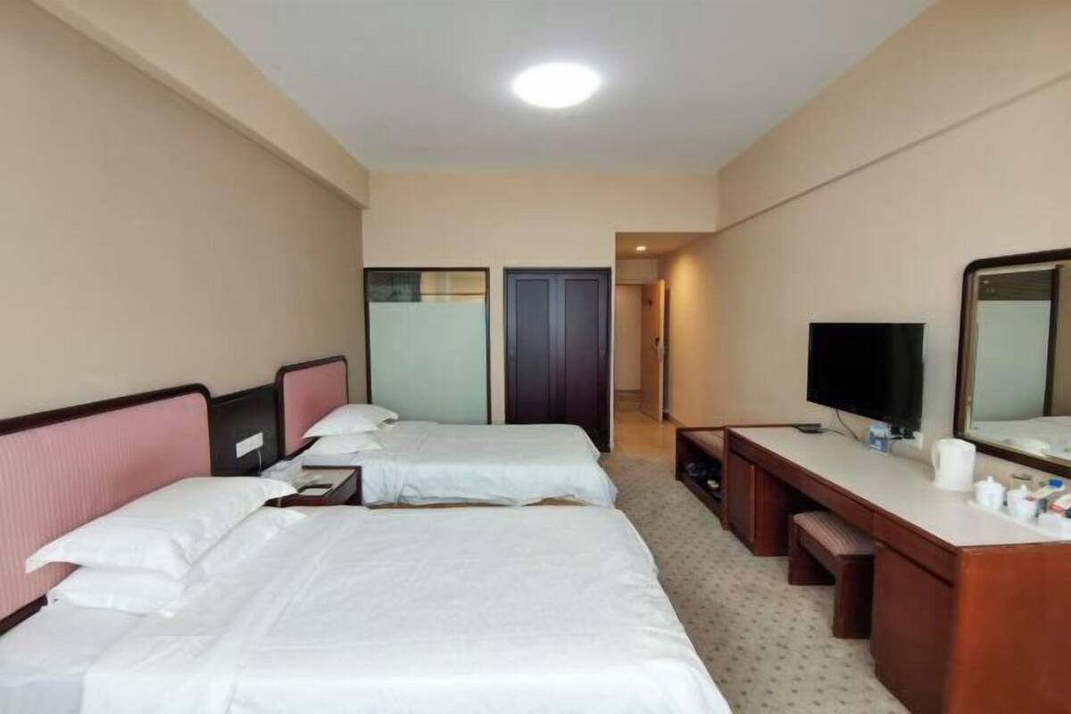 A hotel room with two beds, a desk, a television, and a mirror.