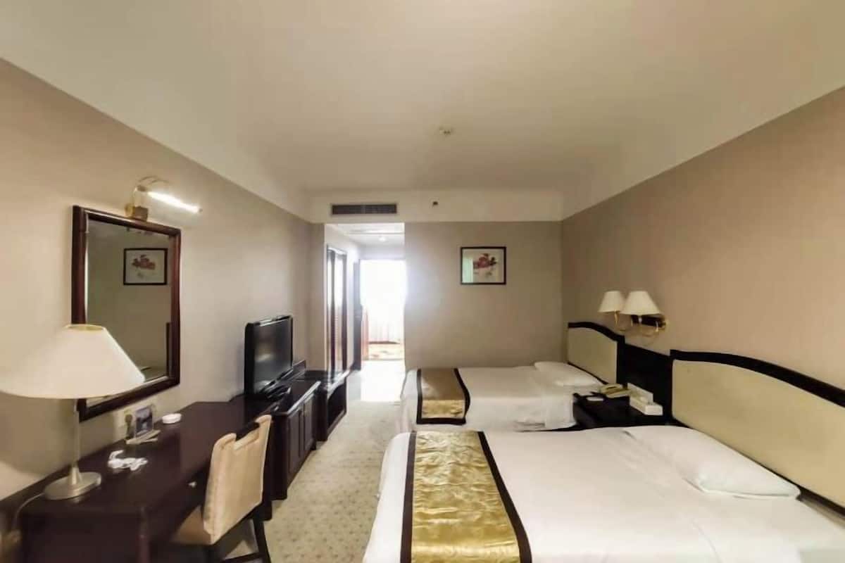 A hotel room with two beds, a desk, a TV, and a mirror.