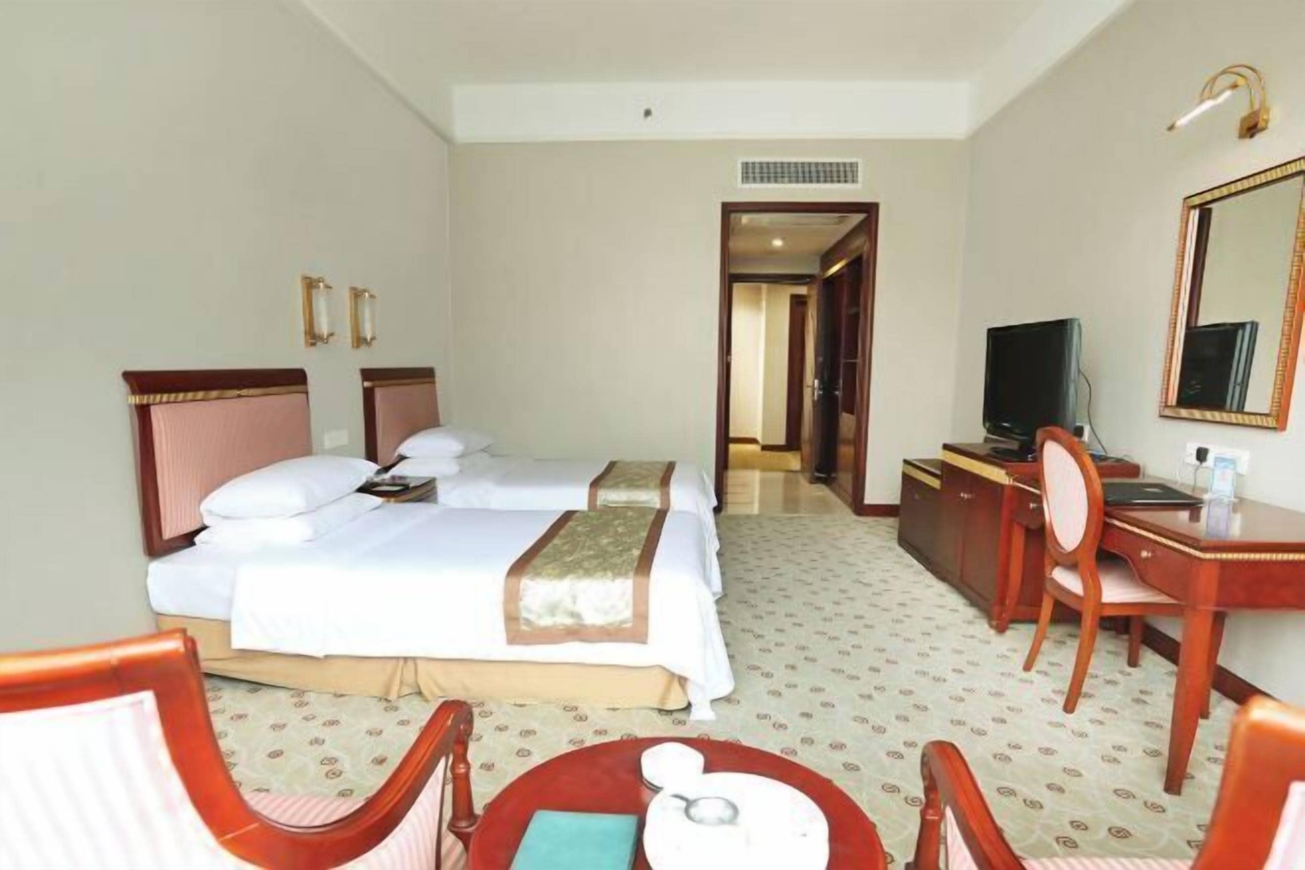 A hotel room with two beds, a desk, a chair, a television, and a mirror.