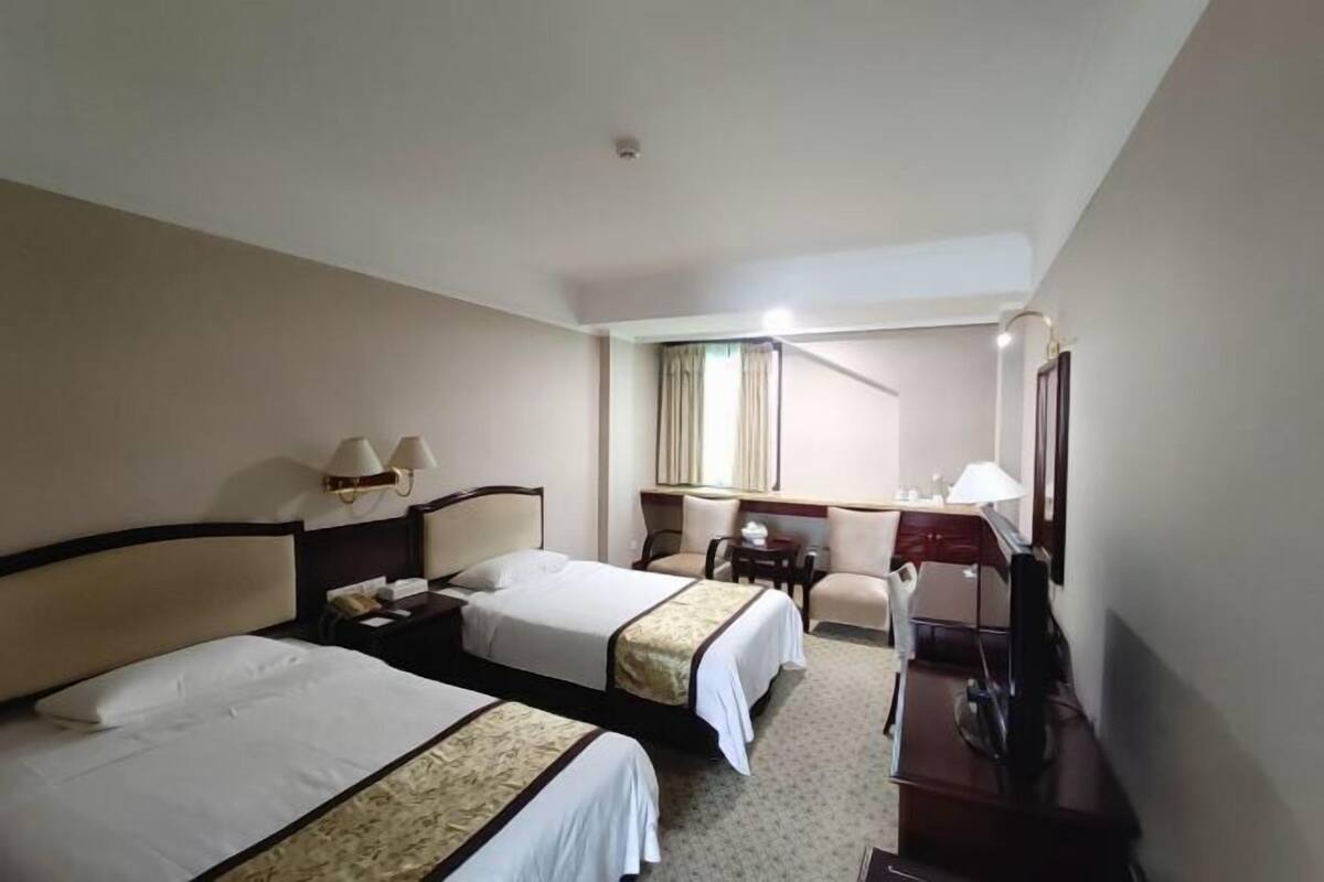 A hotel room with two beds, a desk, a chair, a mirror, and a lamp.