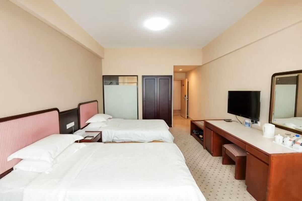 A hotel room with two beds, a desk, a mirror, a television, and a door leading to another room.