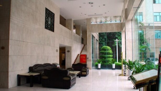 Eine geräumige Lobby mit hoher Decke, einer Treppe, die zu einer oberen Ebene führt, und Blick auf einen gepflegten Garten.
