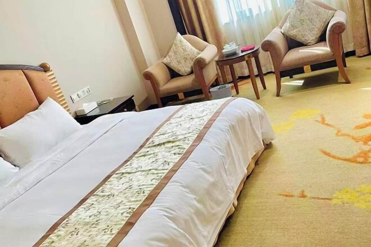 A hotel room with a large bed, two armchairs, a small table, and a carpeted floor.