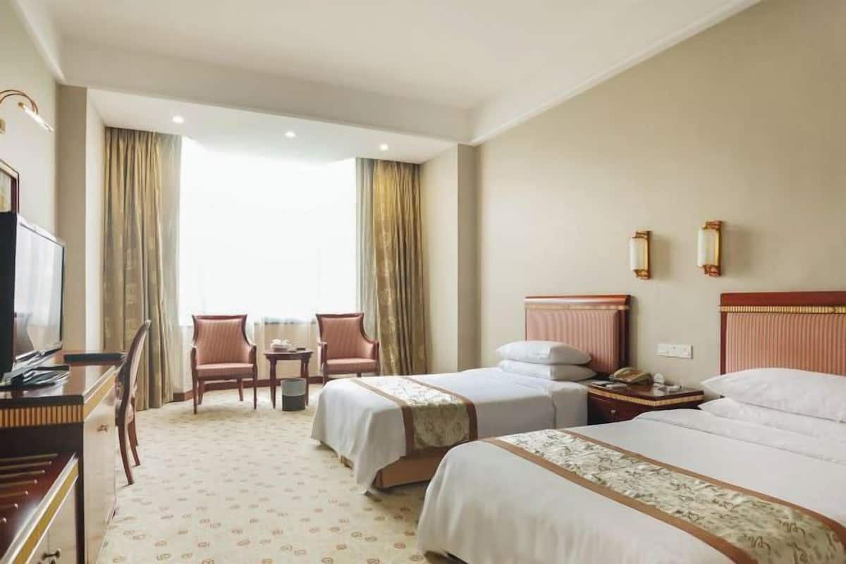 A hotel room with two beds, a desk, a chair, a TV, and a window with curtains.