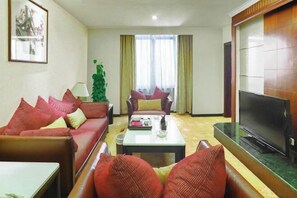 A living room with a sofa set, a coffee table, a TV, and a plant. - Royal Prince Hotel (Quanzhou)