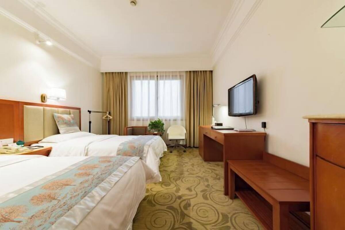 Ein Hotelzimmer mit zwei Betten, einem Schreibtisch, einem Fernseher und einem fenster mit Vorhängen.