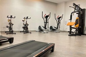 Een fitnessruimte met diverse trainingsapparaten, waaronder loopbanden, hometrainers en krachtapparaten.