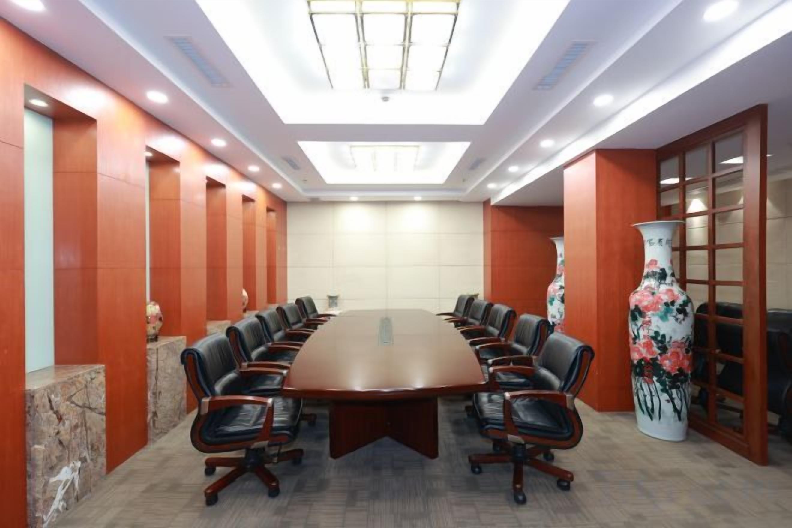 Un salón de conferencias con una gran mesa ovalada, sillas de cuero y un jarrón decorativo.