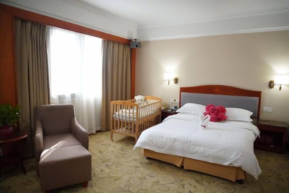 Ein Hotelzimmer mit einem großen Bett, einem Holckrippen, einem Sessel und einem Nachttisch.
