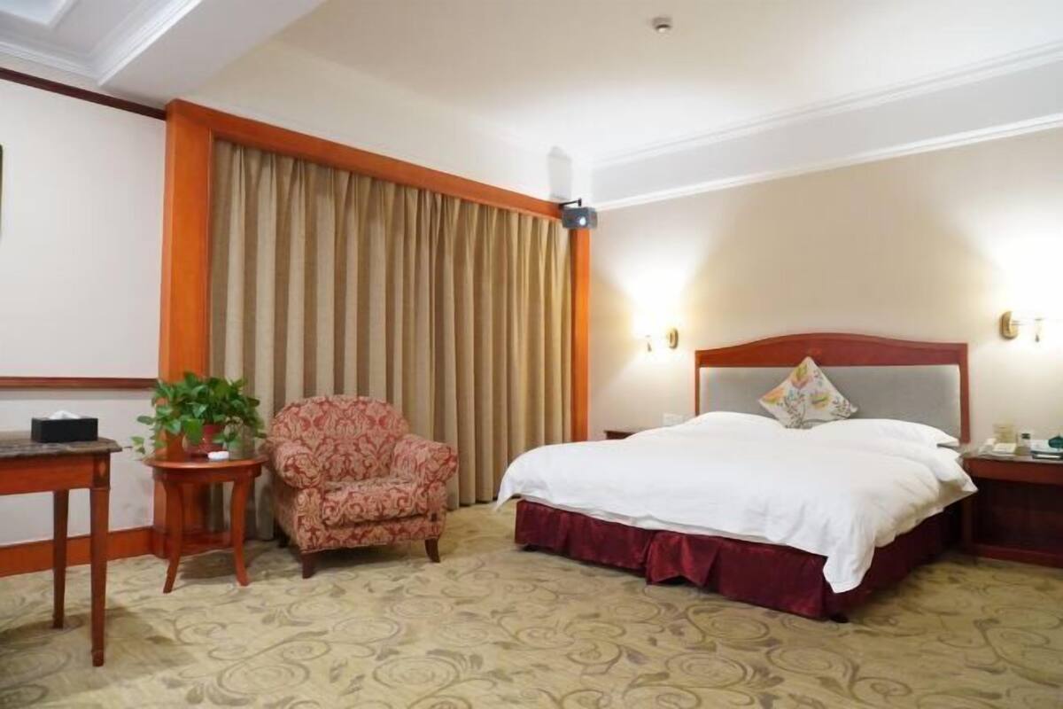 Ein Hotelzimmer mit Bett, Sessel, Tisch und Vorhang.