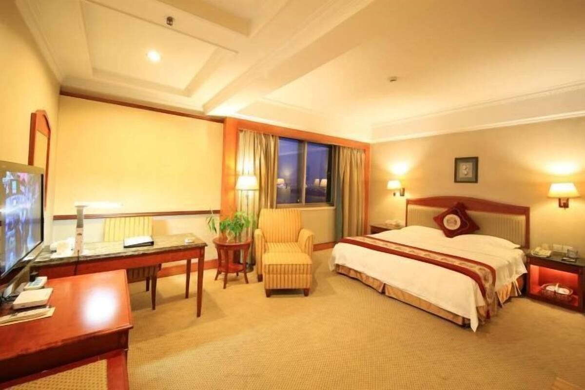 Ein Hotelzimmer mit Bett, Schreibtisch, Stuhl, Fernseher und einem fensterbepflanzten Fenster.