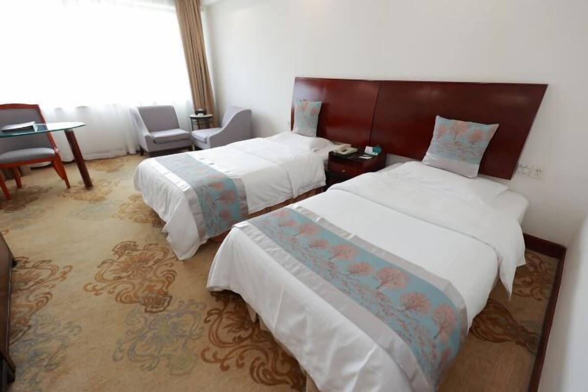 Ein Hotelzimmer mit zwei Betten, einem Schreibtisch, einem Stuhl und Teppichboden.