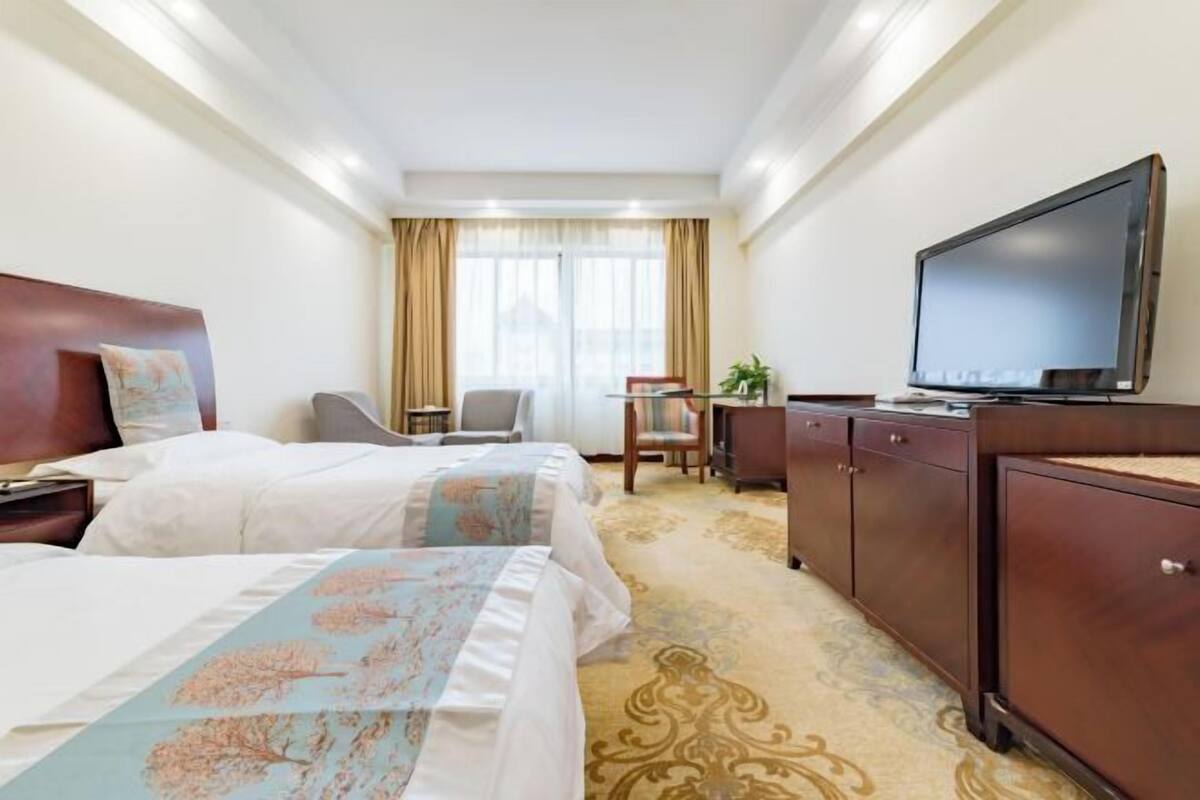 Ein Hotelzimmer mit zwei Betten, einem Fernseher, einem Schreibtisch und einem Stuhl.