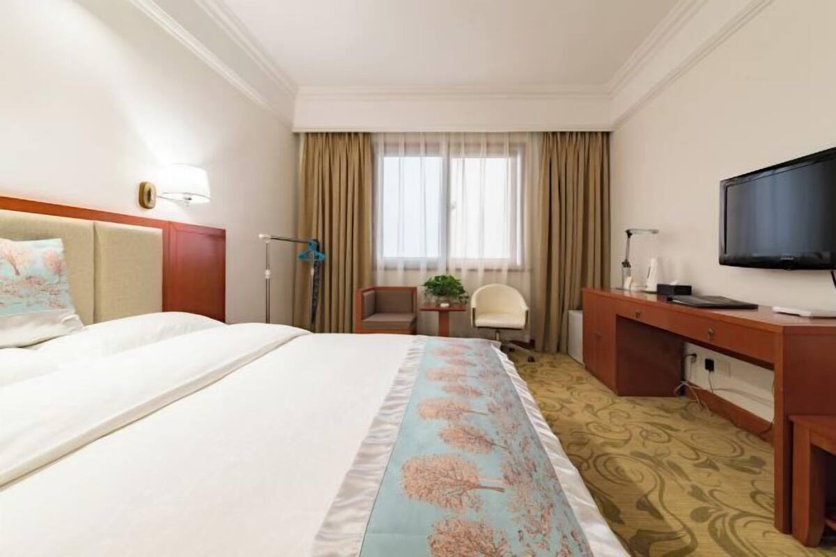 Ein Hotelzimmer mit Bett, Schreibtisch, Fernseher, Sessel und einem Fenster mit Vorhängen.