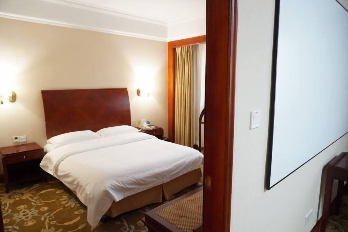 Ein Hotelzimmer mit einem großen Bett, einem Holzkopfteil, einem Nachttisch, einer Lampe und einem Spiegel.